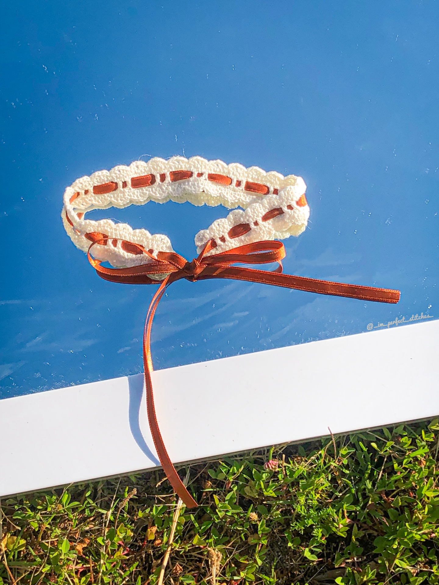Colar de crochê branco com fita castanha amarrada em laço sobre superfície azul