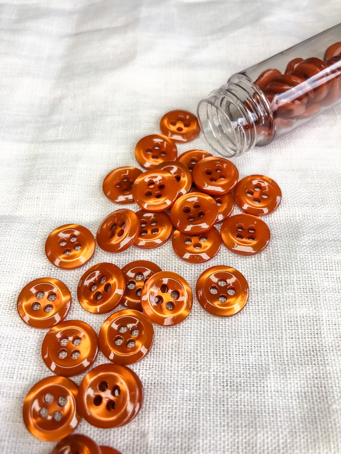 Botões de plástico laranja brilhante com quatro furos sobre tecido branco e em frasco