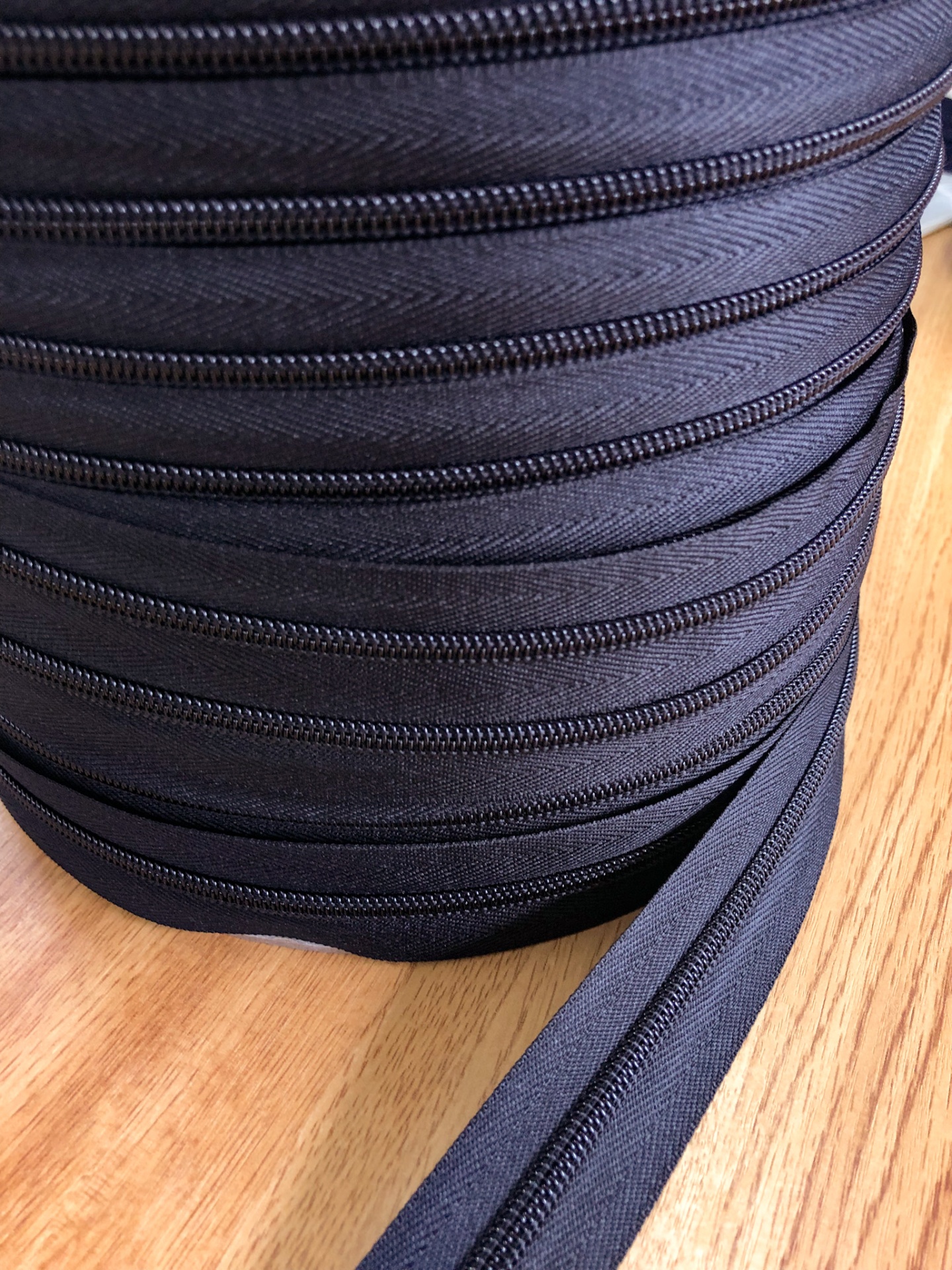 Rolo de fechos éclair pretos com padrão espinha de peixe sobre madeira