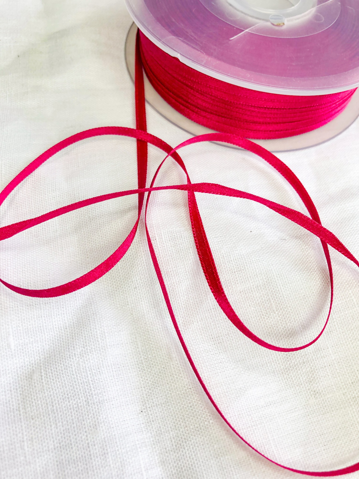 Rolo de fita rosa fúcsia estreita sobre tecido branco