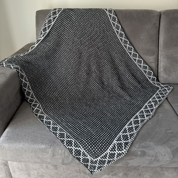 Cobertor preto, cinza e branco com padrão geométrico sobre sofá cinza