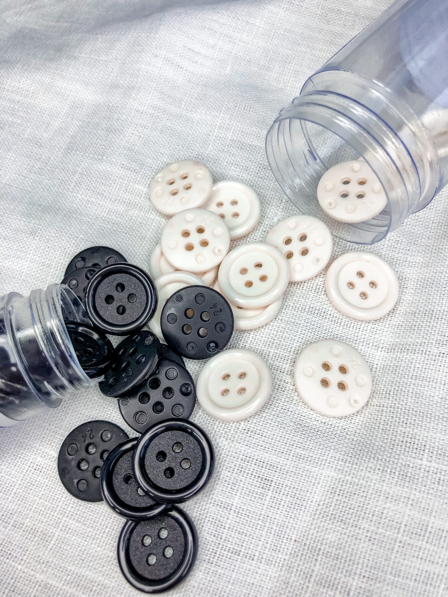 Botões de plástico preto e branco em tecido branco com frascos plásticos.