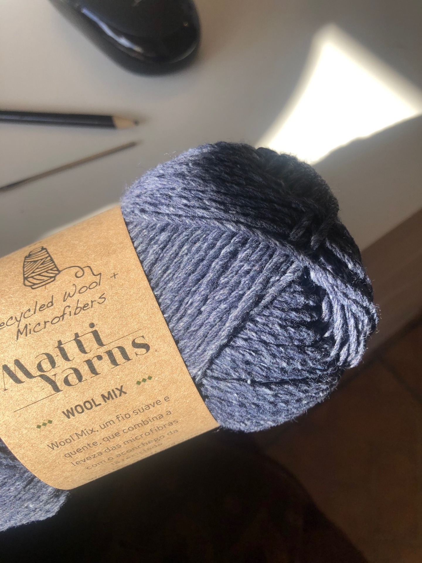 Novelo de lã azul escuro com etiqueta de papel pardo em mesa branca
