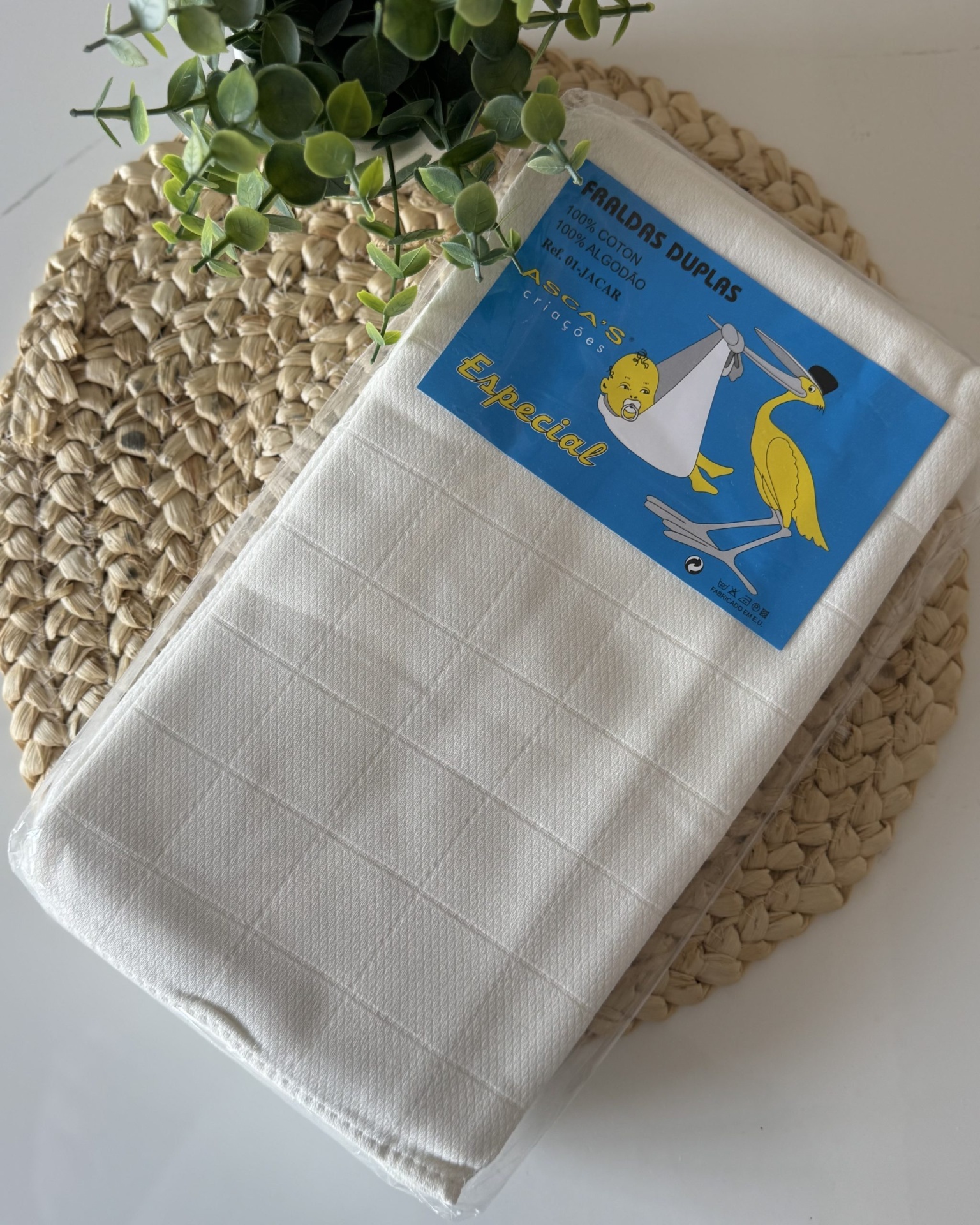 Fralda branca de tecido com etiqueta azul ilustrativa de cegonha segurando bebé