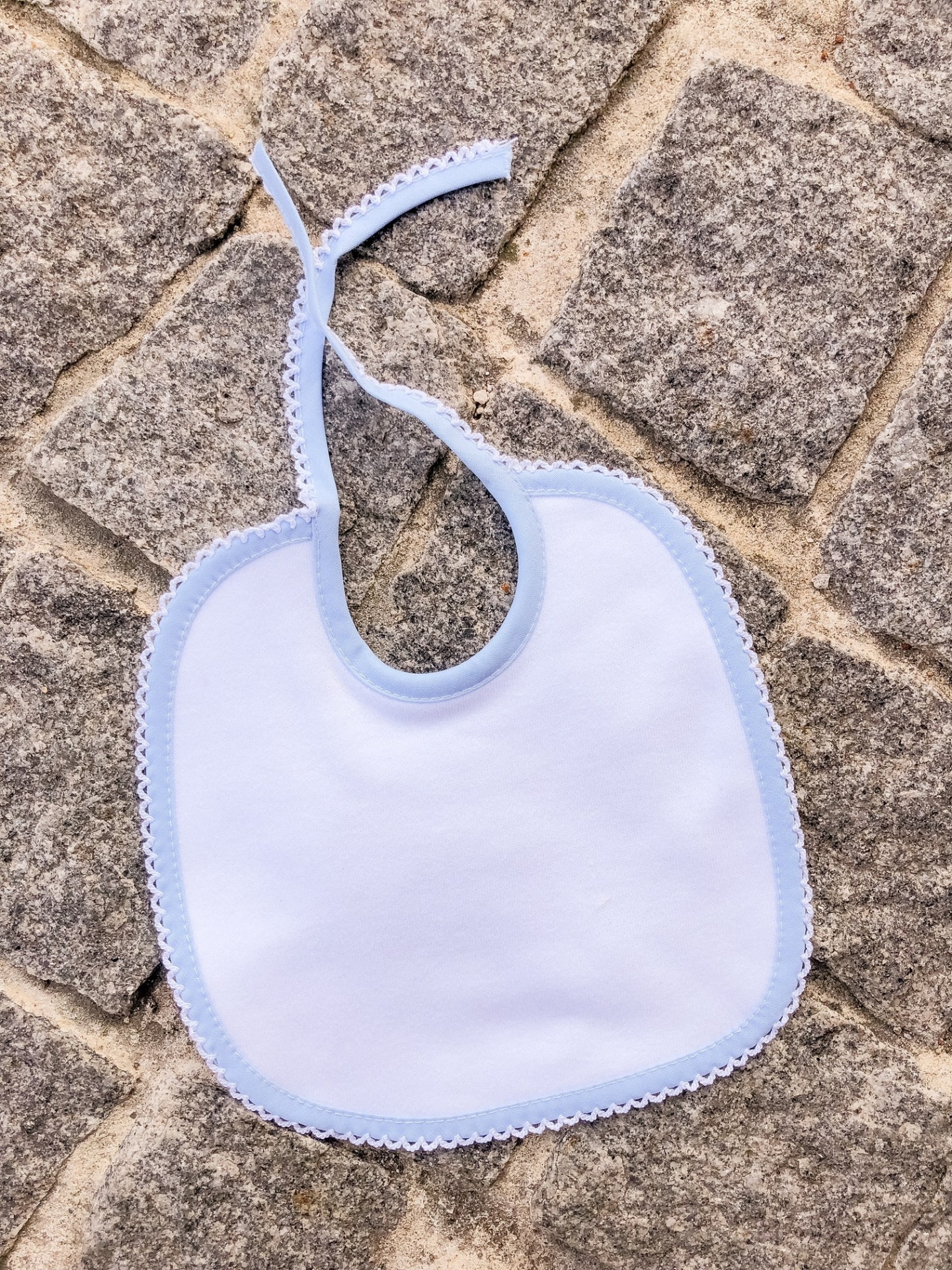Babete branco com borda azul claro em pavimento de pedras cinzentas