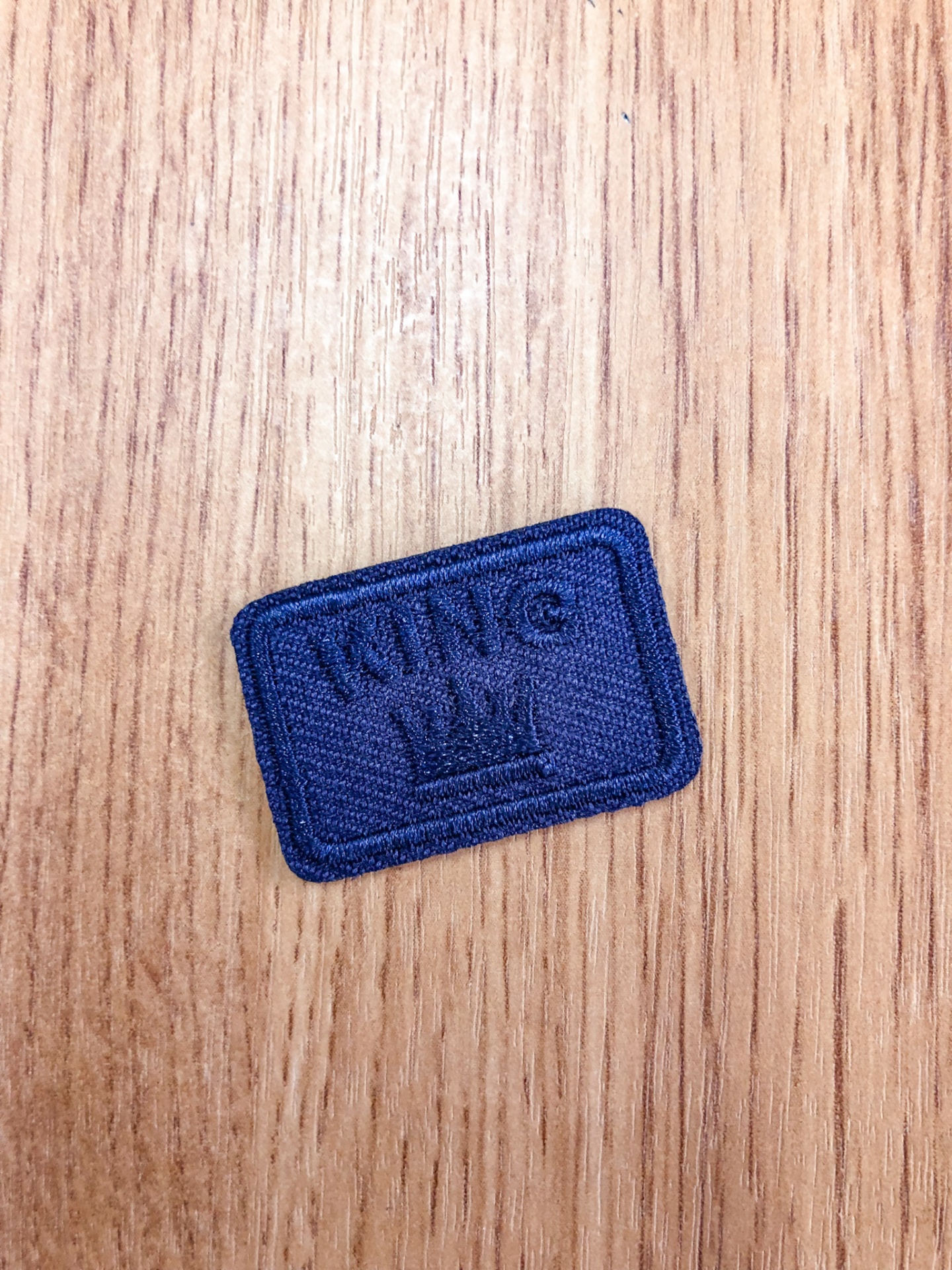 Parche tecido azul com bordado KING e coroa sobre madeira