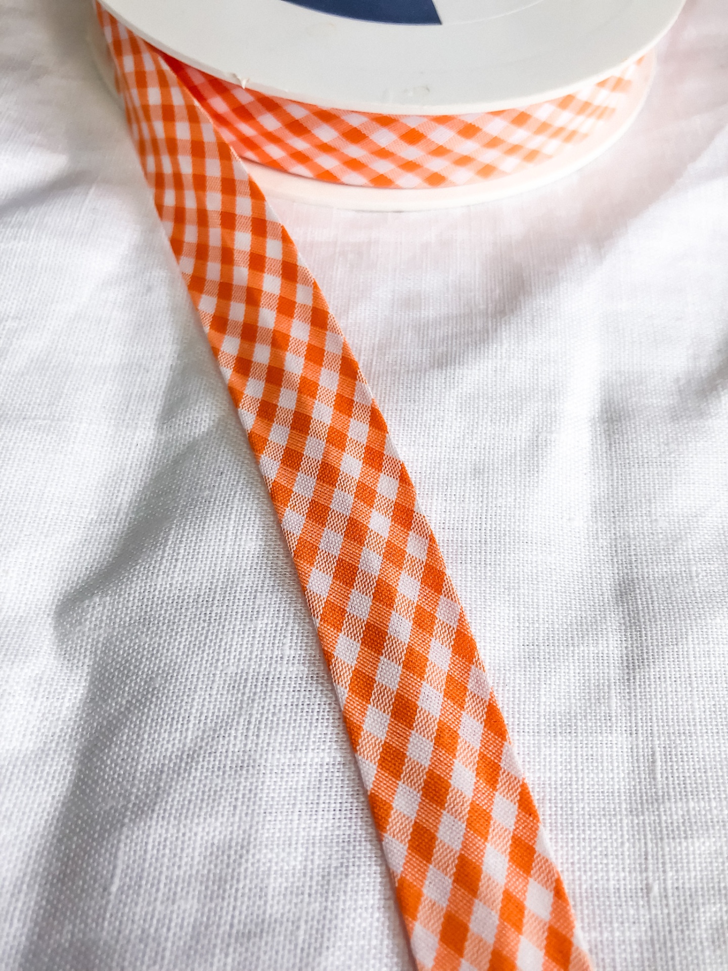 Fita xadrez laranja e branco em carretel sobre tecido branco