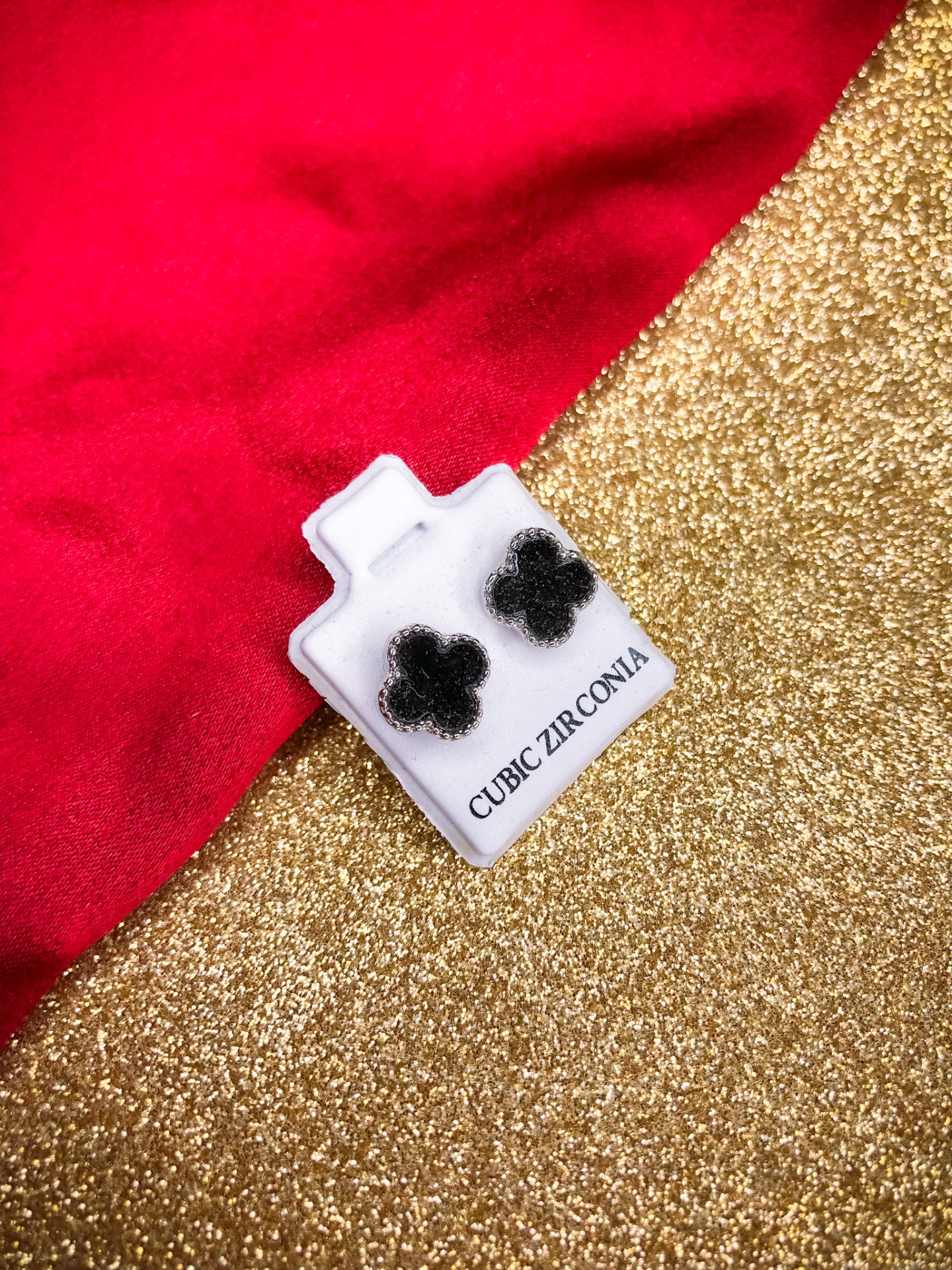 Brincos de zircônia cúbica preta em cartão branco sobre tecido vermelho e fundo dourado