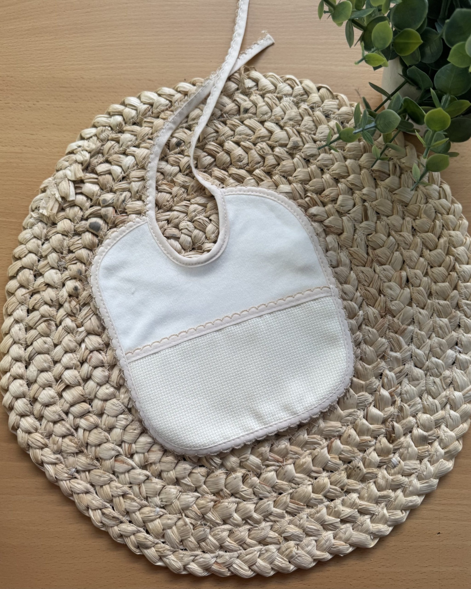 Babete branco creme com acabamento rosa em tapete redondo de corda sobre mesa de madeira clara