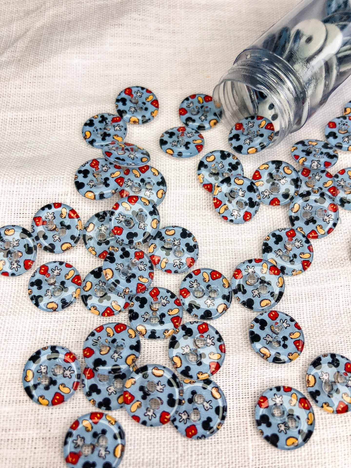 Botões redondos azuis coloridos espalhados em tecido branco a partir de frasco plástico