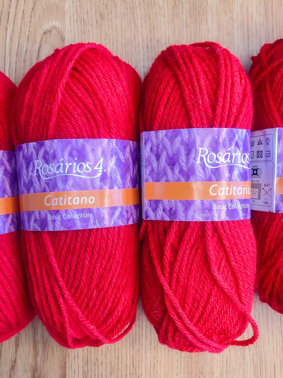 Novelos de lã vermelha Rosários 4 Catitano com etiquetas roxas sobre madeira.