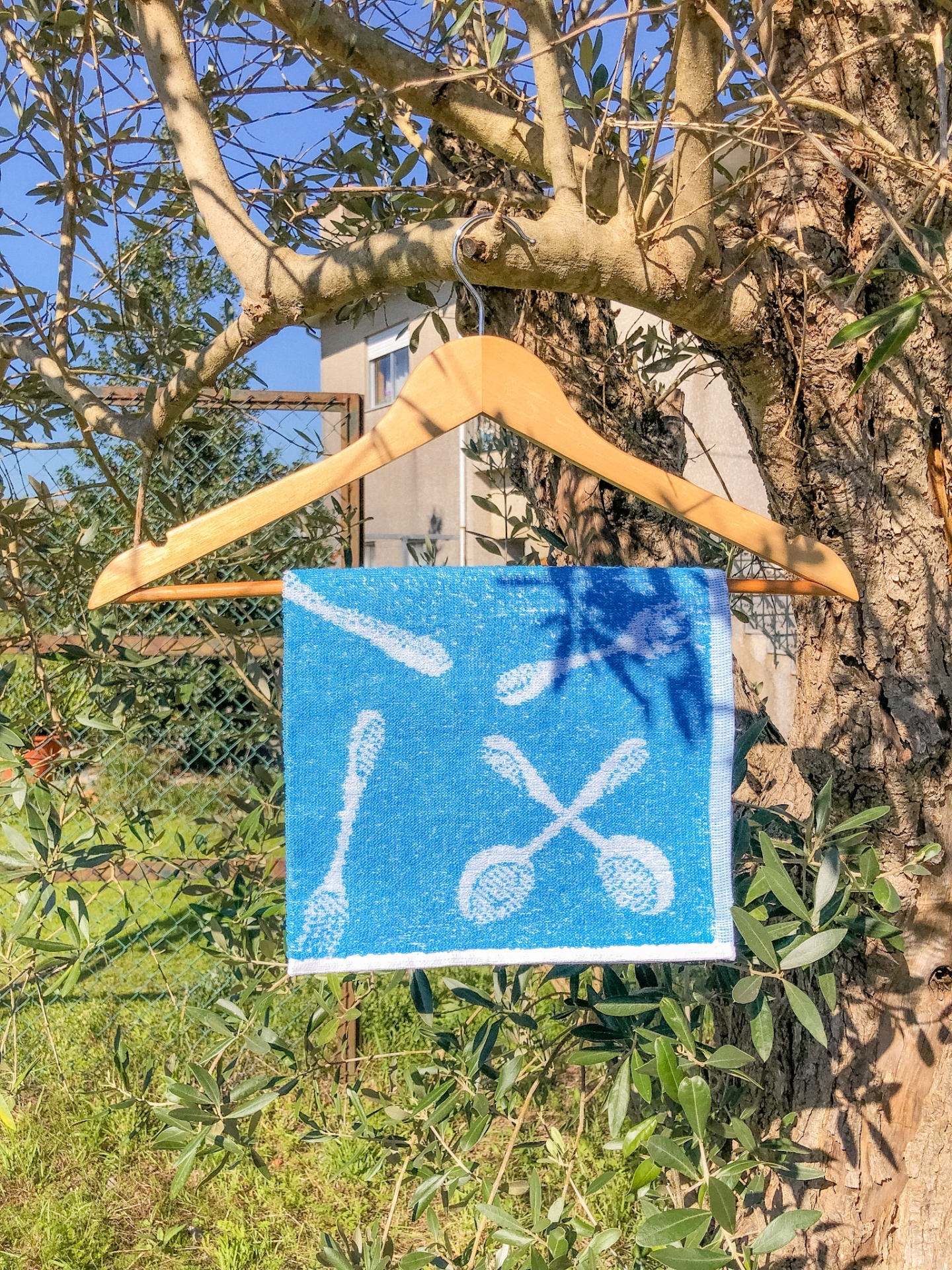 Pano azul com padrões brancos pendurado num cabide de madeira na árvore
