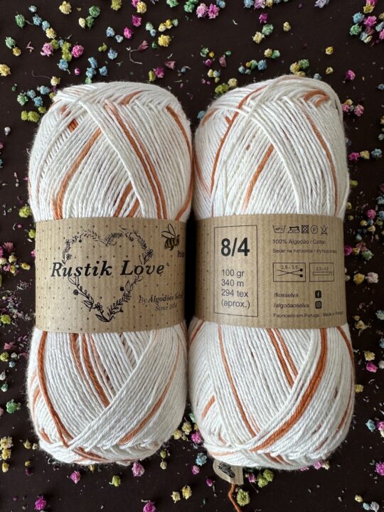 Dois novelos de fio de algodão branco com listras laranja e etiqueta Rustik Love