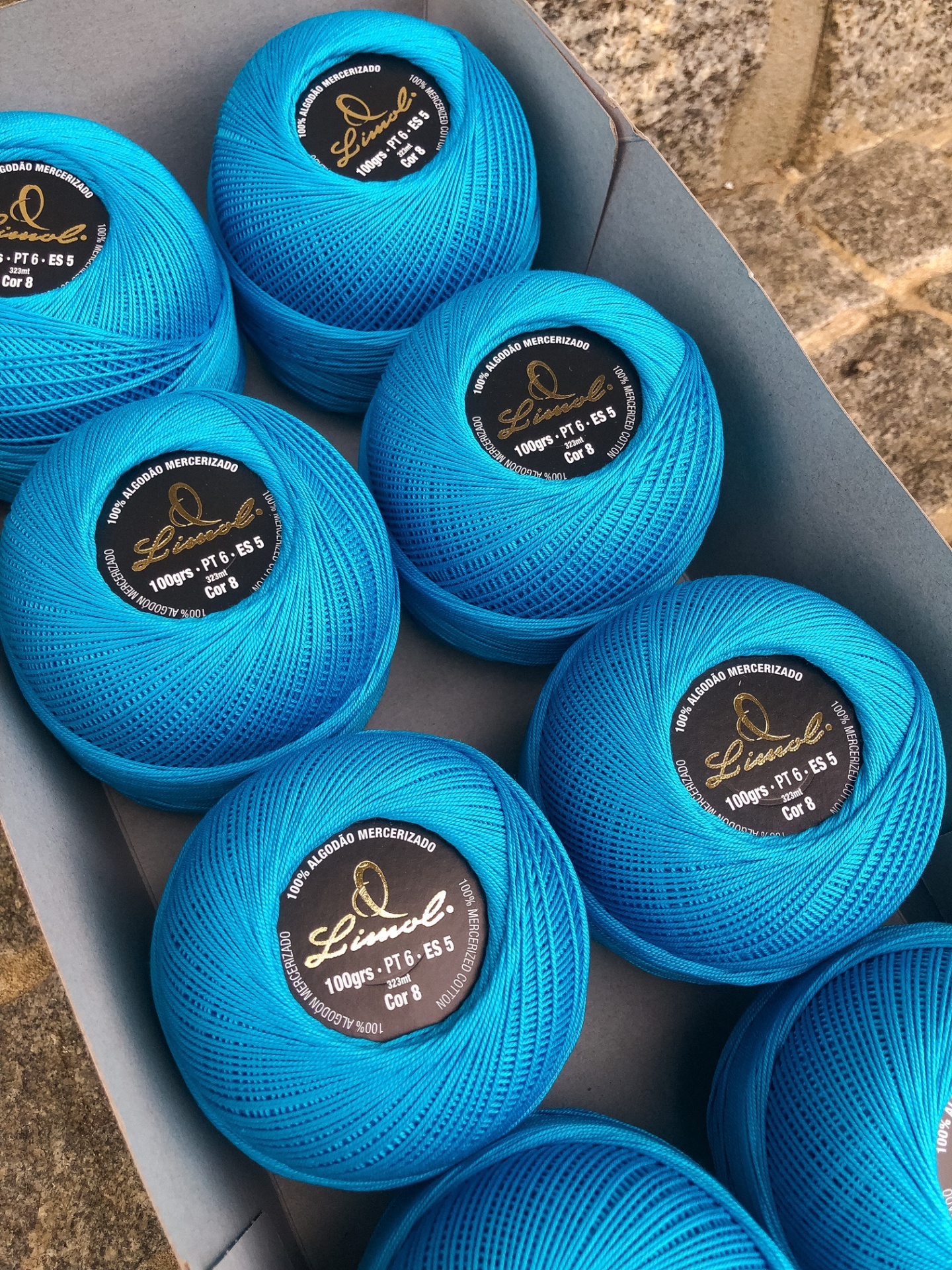 Novelos de linha azul com etiquetas pretas dentro de caixa cinzenta