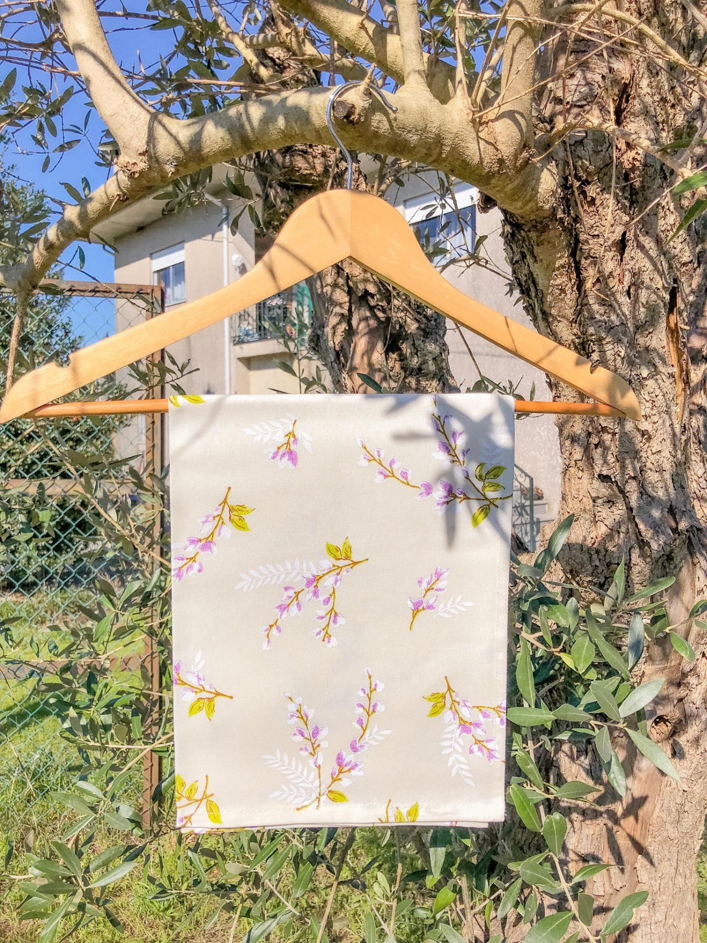 Guardanapo branco com flores rosa e verdes pendurado num cabide de madeira ao ar livre