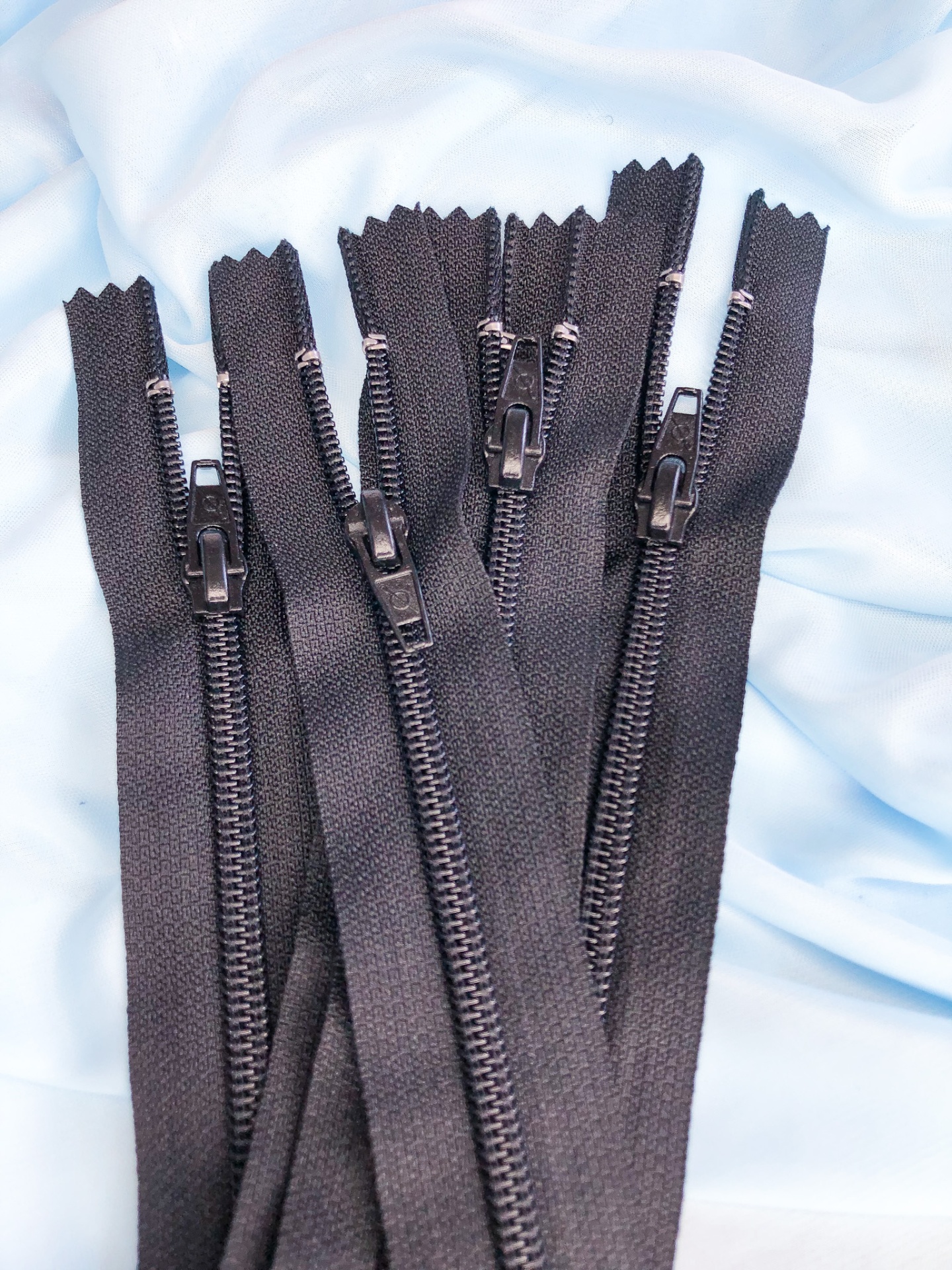 Fechos de correr pretos com dentes de plástico e puxadores pretos sobre tecido azul claro