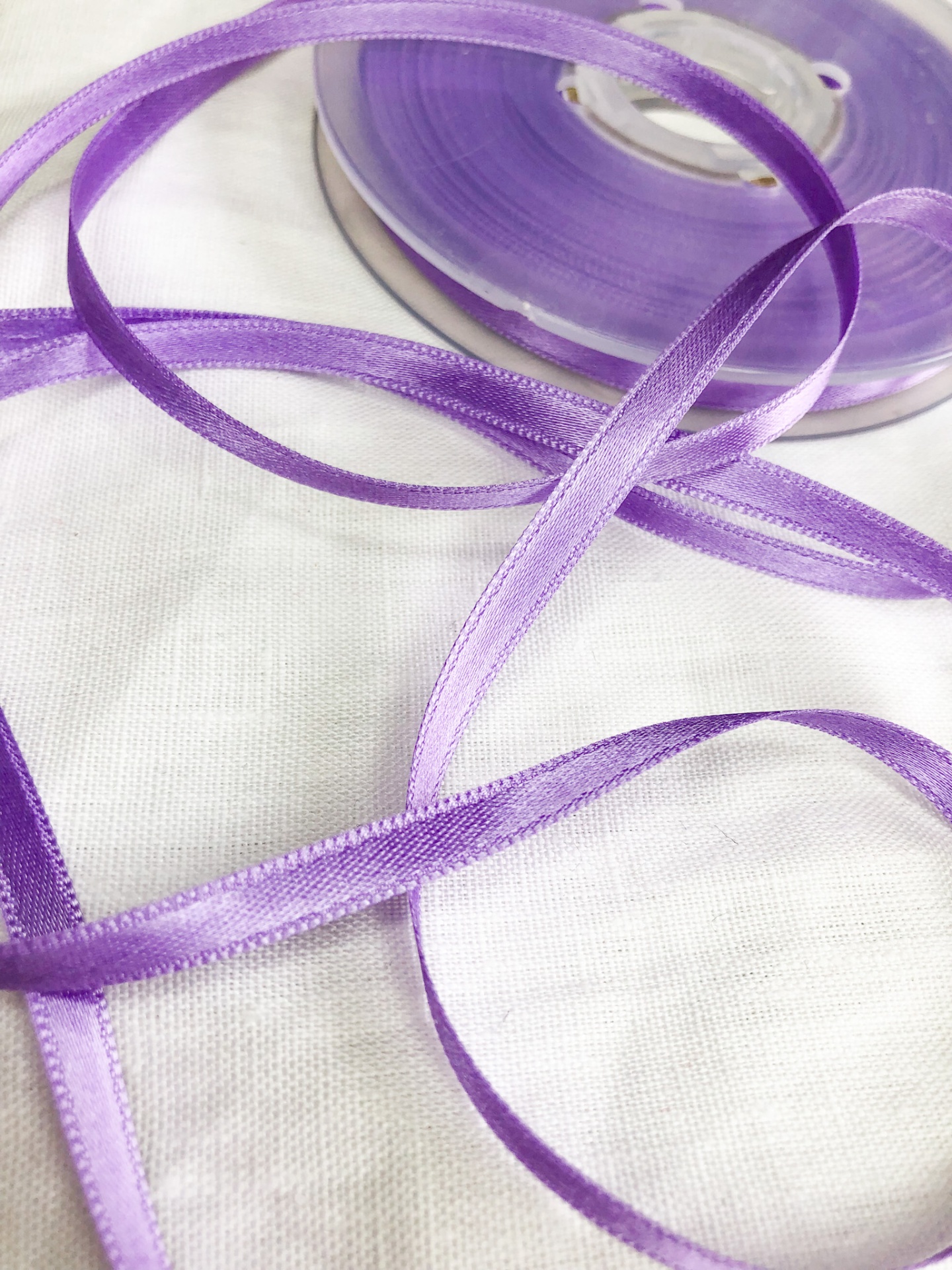 Fita de cetim roxa estreita enrolada em carretel sobre tecido branco
