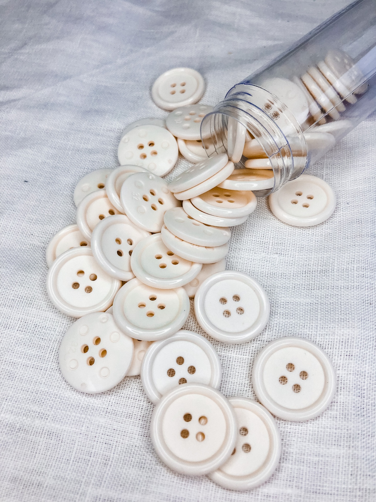 Botões brancos redondos com quatro furos em tecido branco e tubo plástico aberto