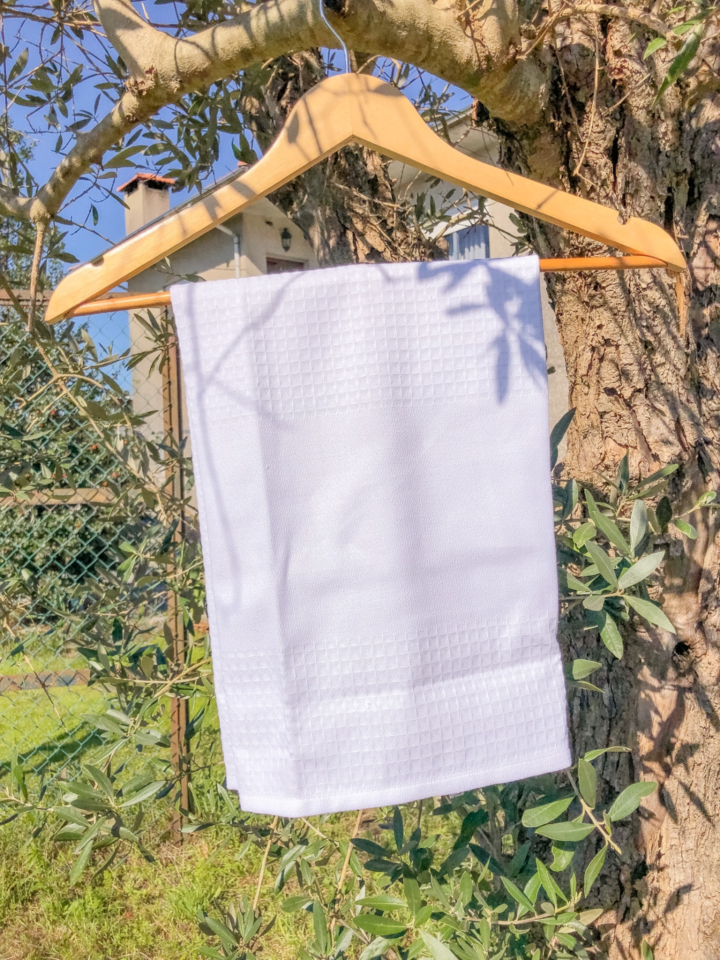 Toalha branca pendurada num cabide de madeira numa árvore ao ar livre