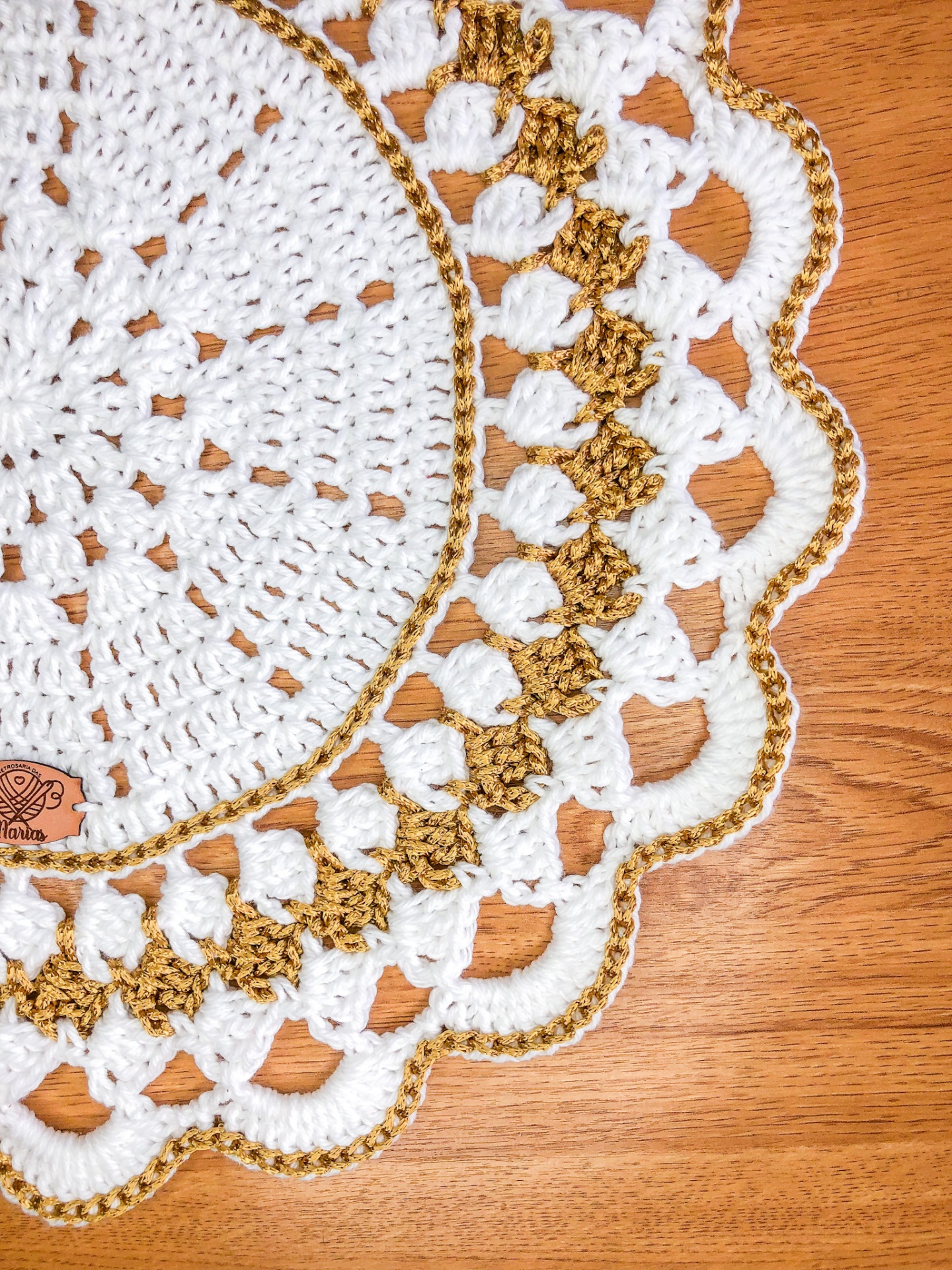 Toalha de crochê branca e castanho-ouro com padrão ondulado sobre madeira clara
