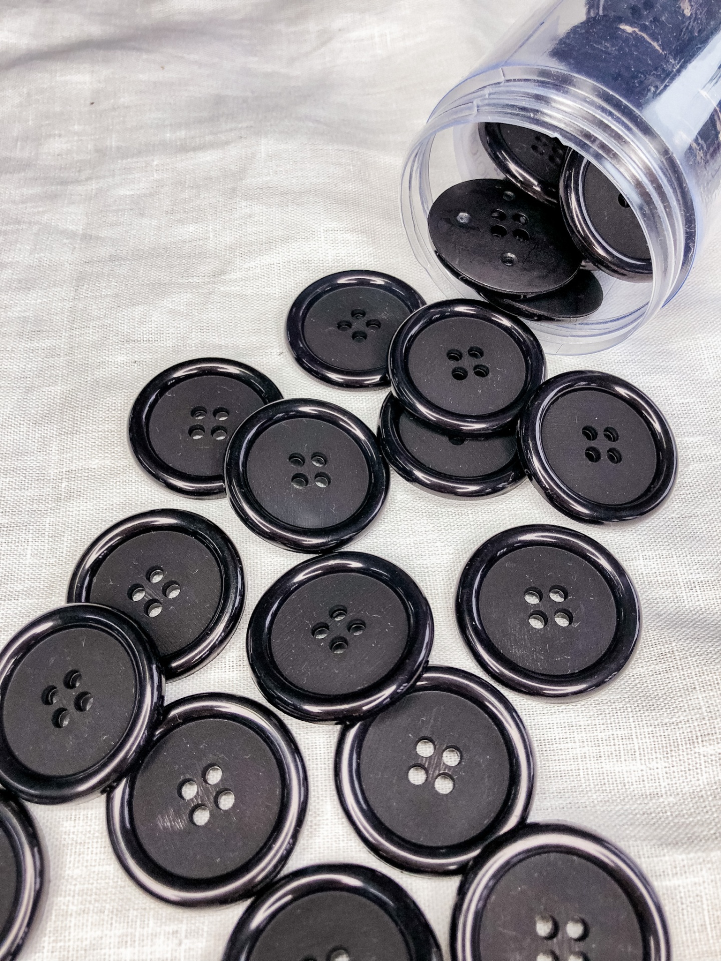 Botões pretos de plástico com quatro furos sobre tecido branco