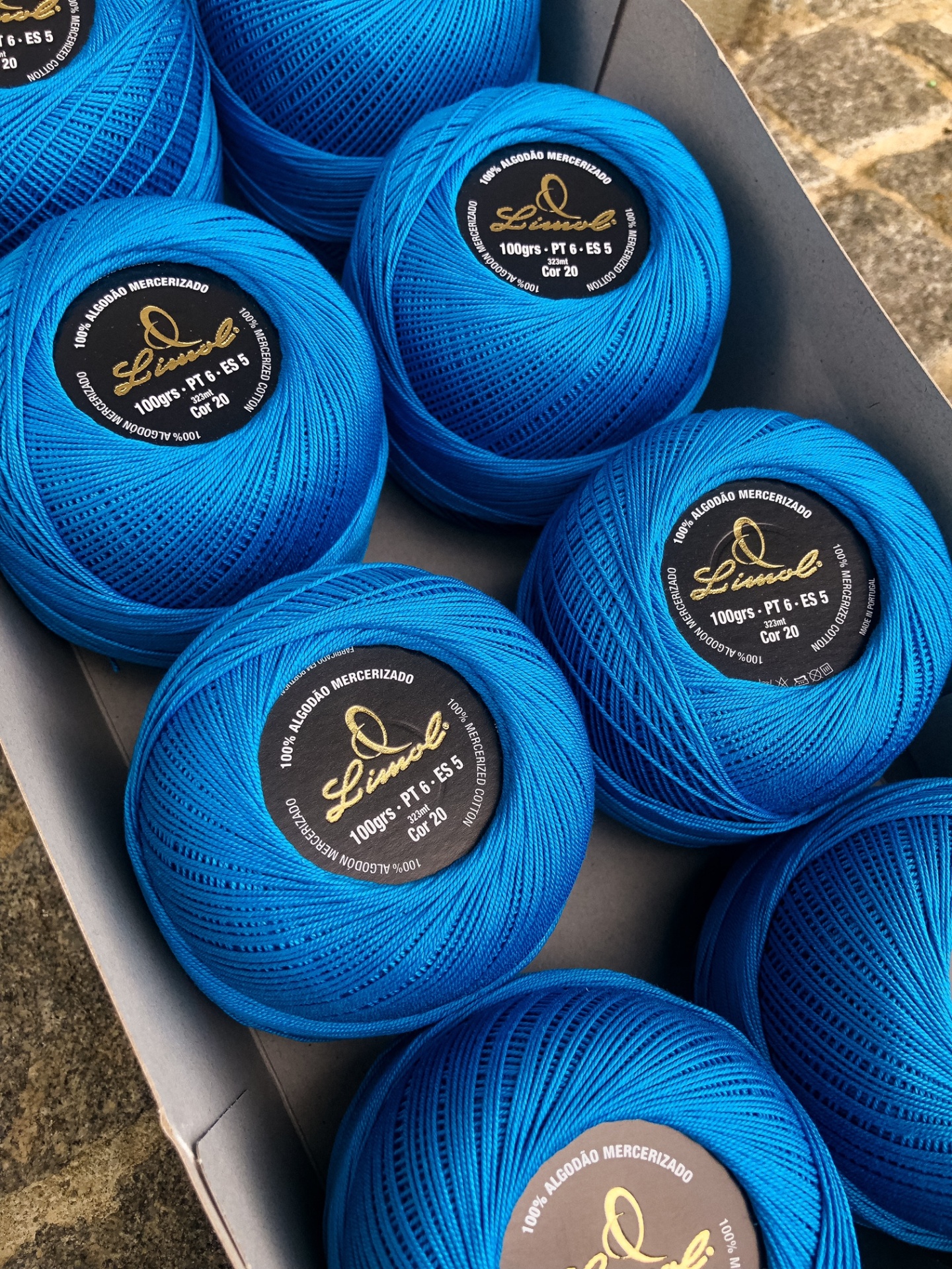 Novelos de fio azul-turquesa mercerizado embalados numa caixa cinzenta