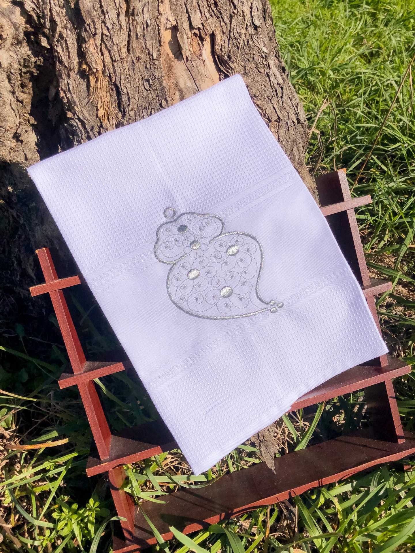 Toalha branca bordada com rato cinza com brilhantes, posto sobre suporte de madeira em ambiente ao ar livre