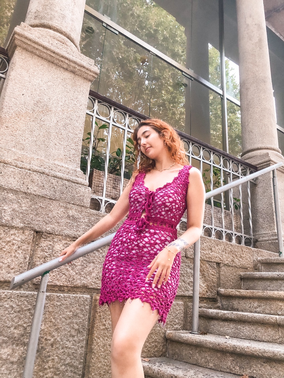 Mulher com vestido de croché rosa numa escada de pedra ao ar livre