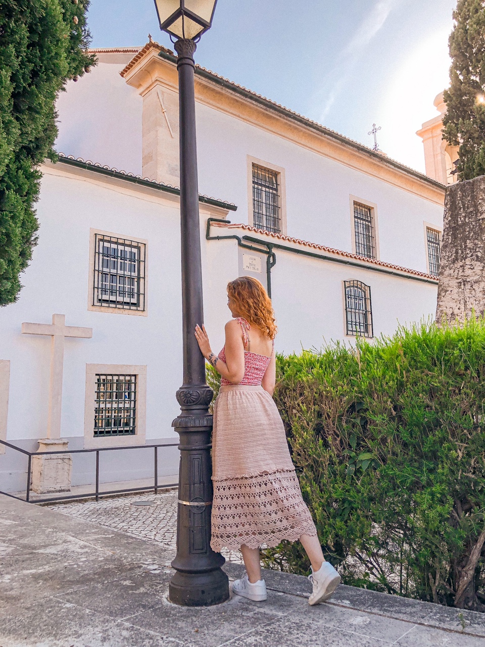 Mulher de costas junto a um candeeiro preto com saia rendada rosa e top cor-de-rosa