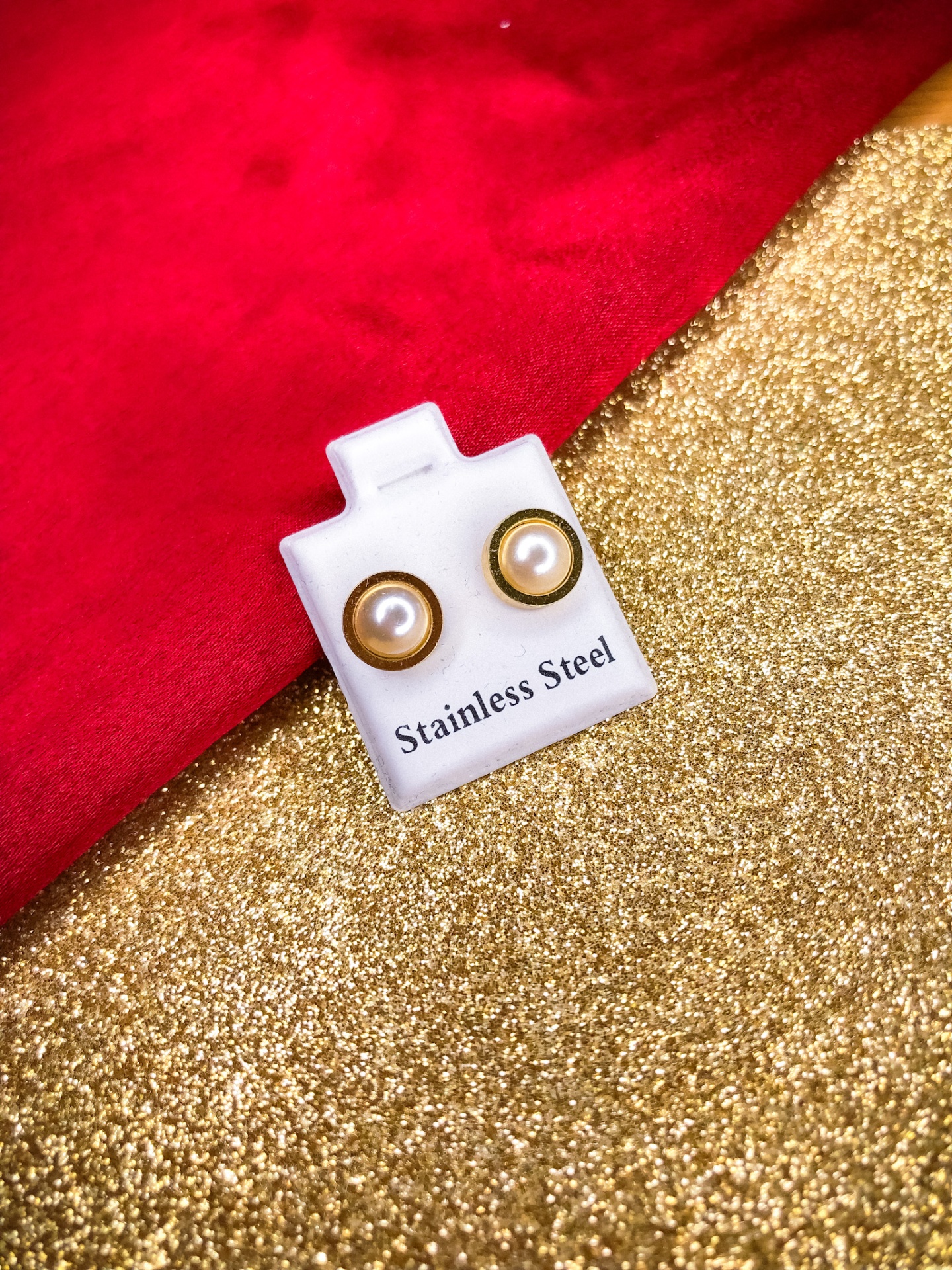 Brincos com pérola e dourado em base branca com texto, sobre fundo dourado e vermelho.