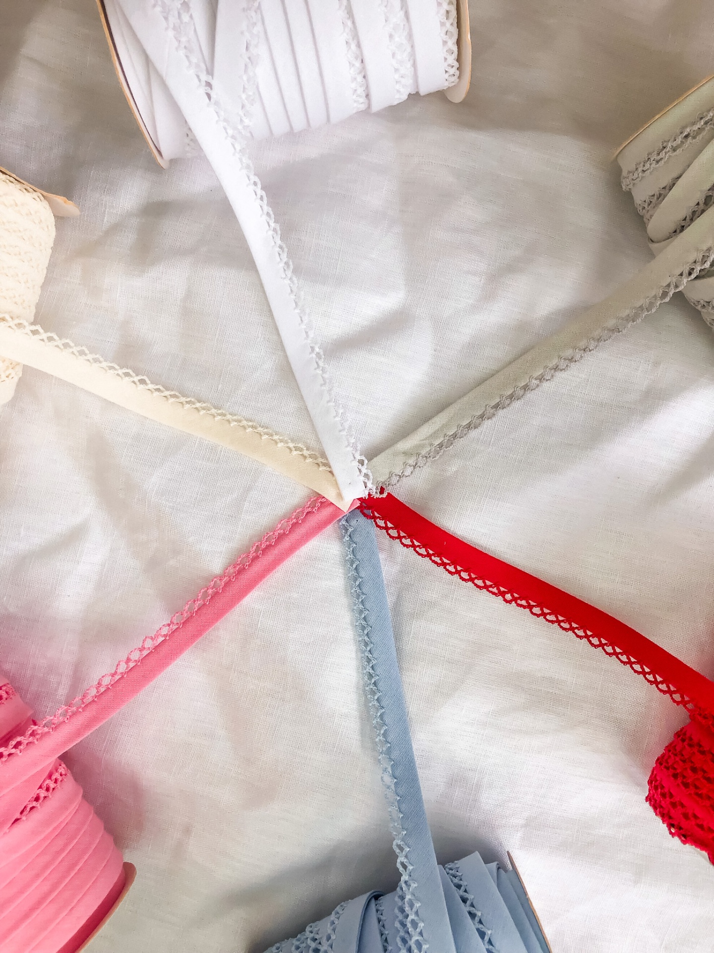 Vários rolos de fitas decorativas coloridas com bordas rendadas sobre tecido branco