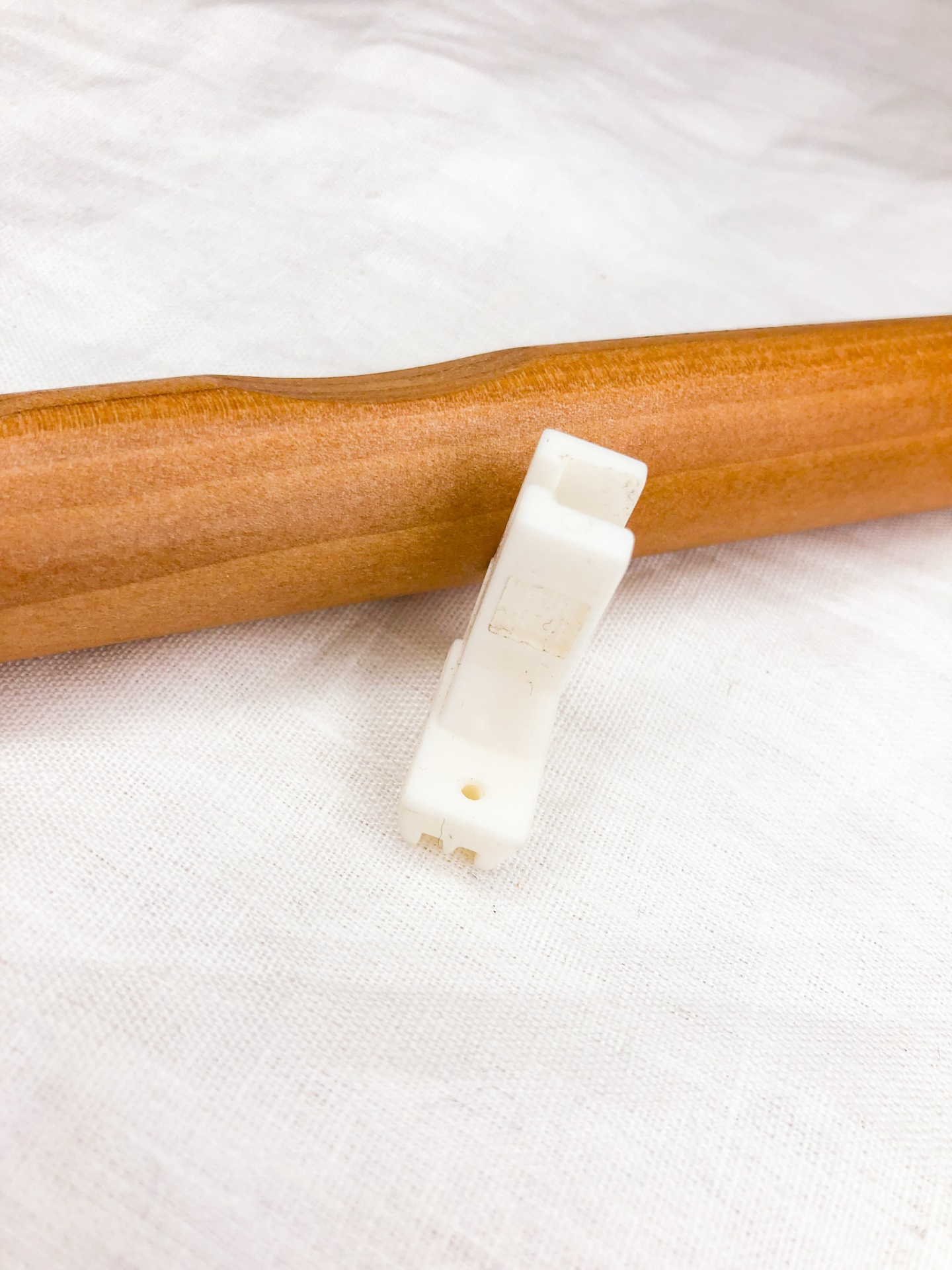 Cabide de madeira com pequeno objeto plástico branco sobre tecido branco