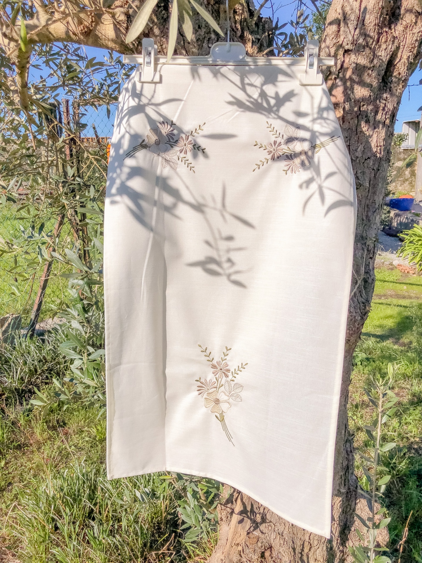 Saia branca com bordados florais pendurada numa árvore ao ar livre