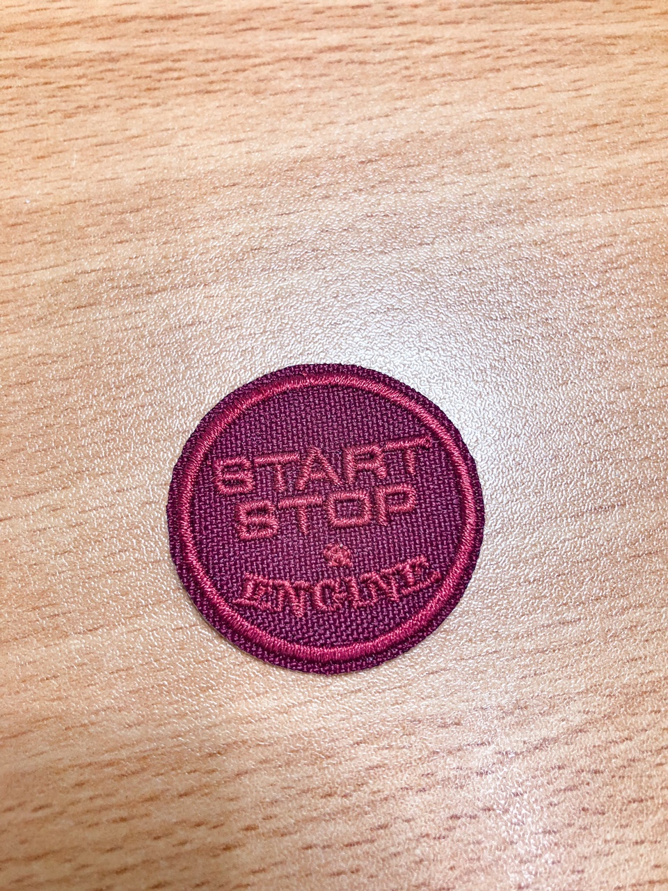 Emblema redondo bordô com texto START STOP ENGINE em tecido sobre madeira clara