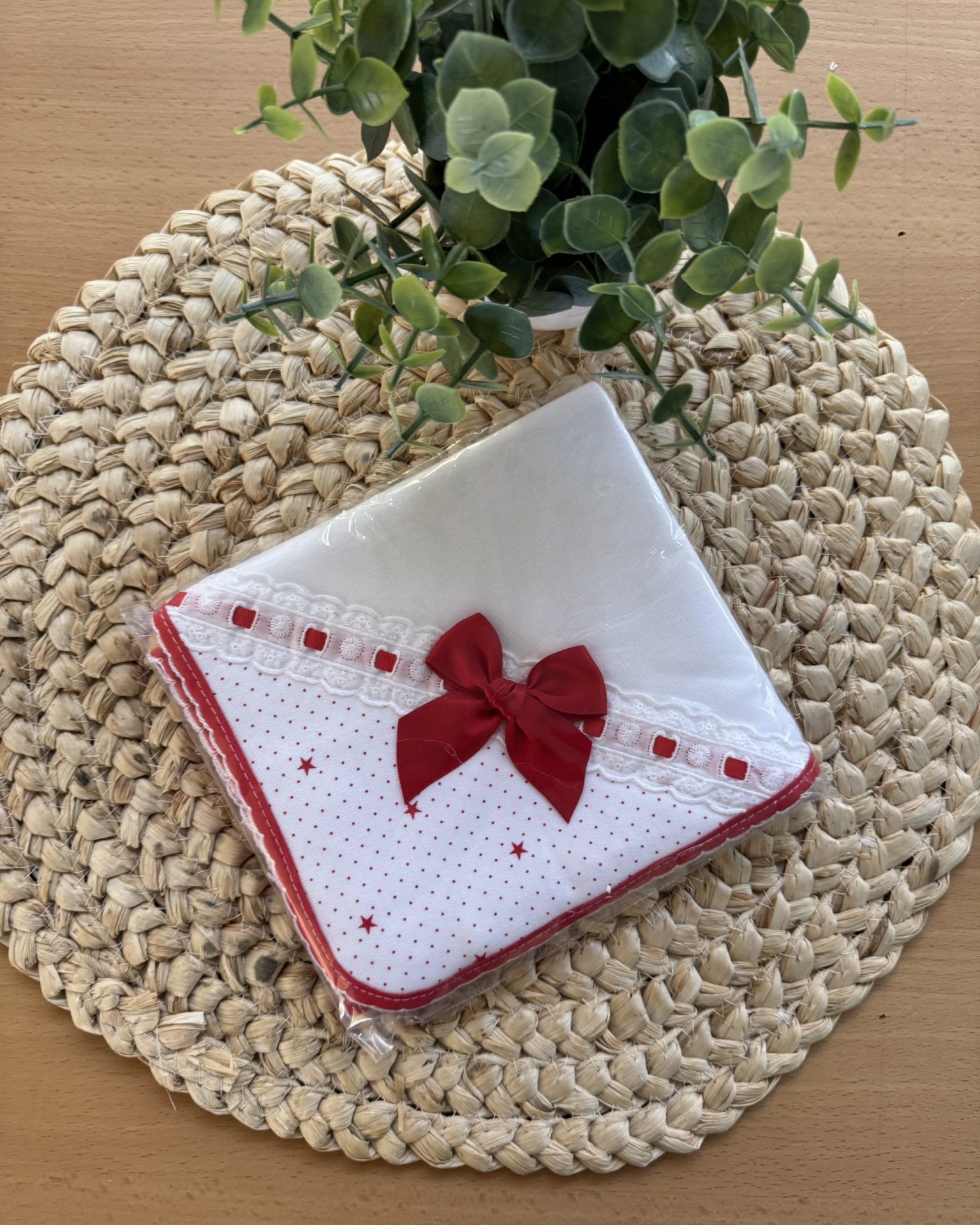 Toalha branca com laço vermelho sobre suporte trançado com planta ao fundo