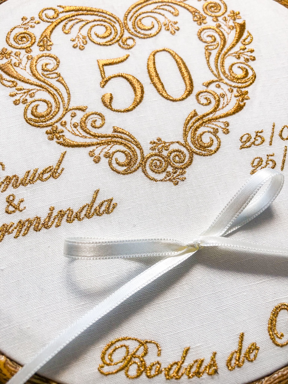 Tecido branco bordado em dourado com número 50 e laço branco