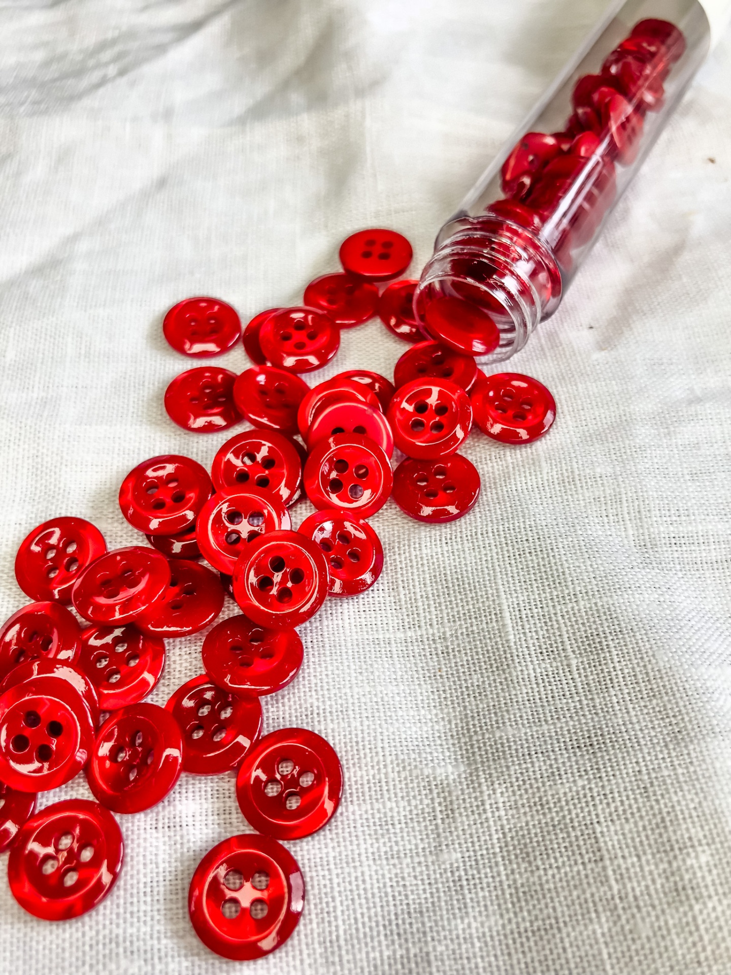 Botões vermelhos pequenos em tubo plástico e sobre tecido branco