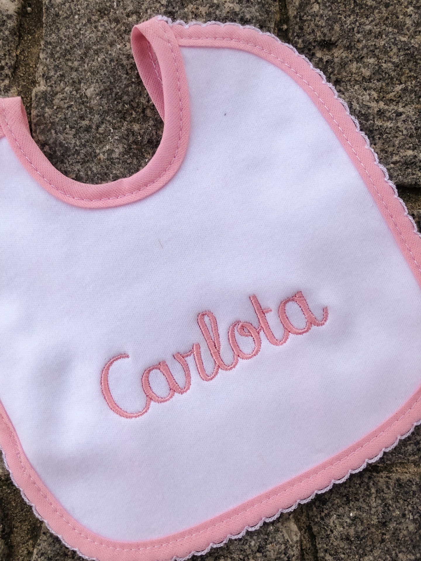 Babete branco com bordas cor de rosa e bordado com o nome Carlota