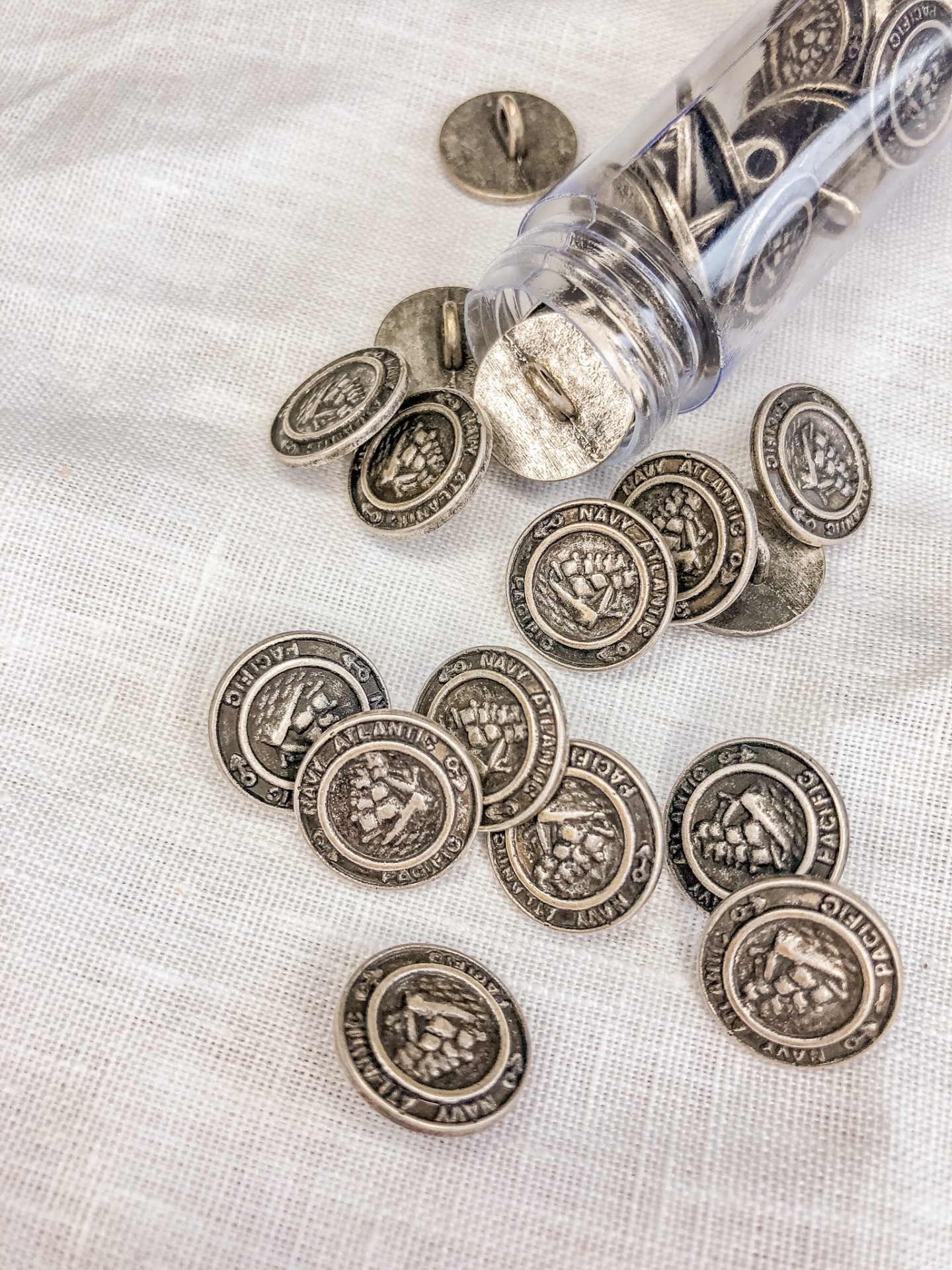 Botões metálicos redondos com escudo, sobre tecido branco, junto a recipiente plástico