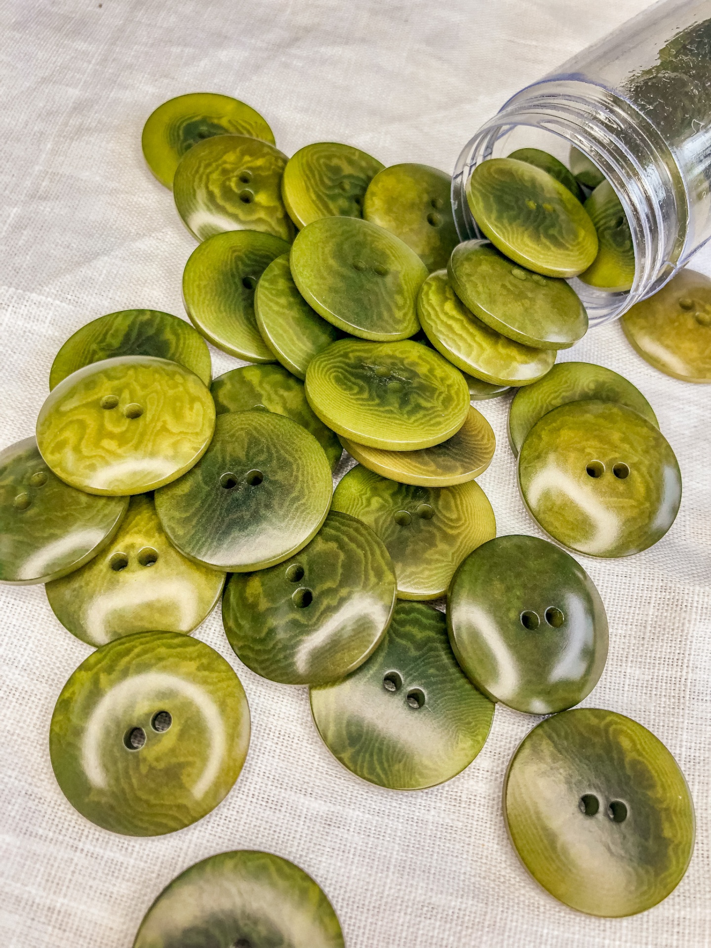 Botões redondos verdes com padrão marmoreado e dois furos, sobre tecido e frasco transparente
