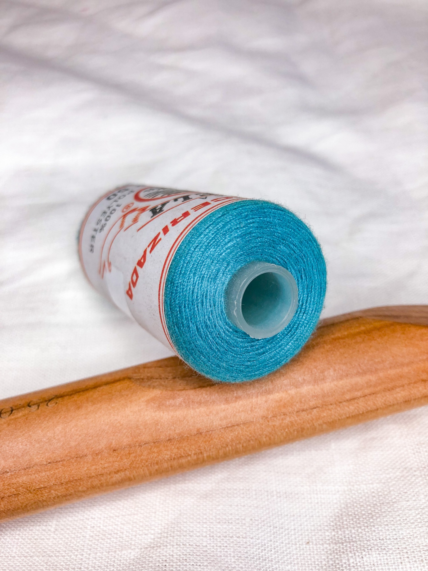 Rolo de linha azul turquesa com rótulo branco e vermelho, colocado sobre superfície de madeira castanha clara.