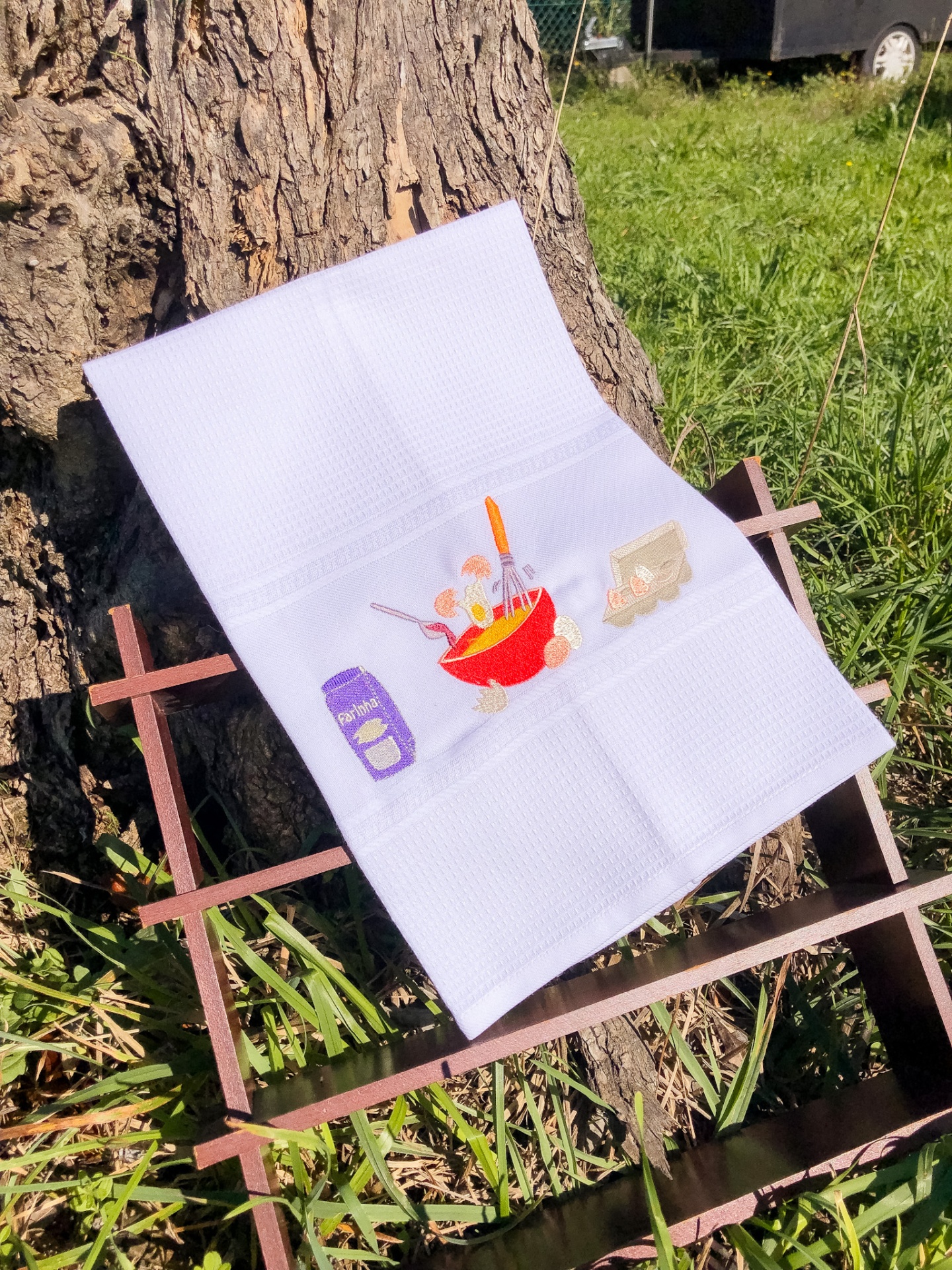 Toalha branca com ilustrações de cozinha apoiada em suporte de madeira junto a árvore