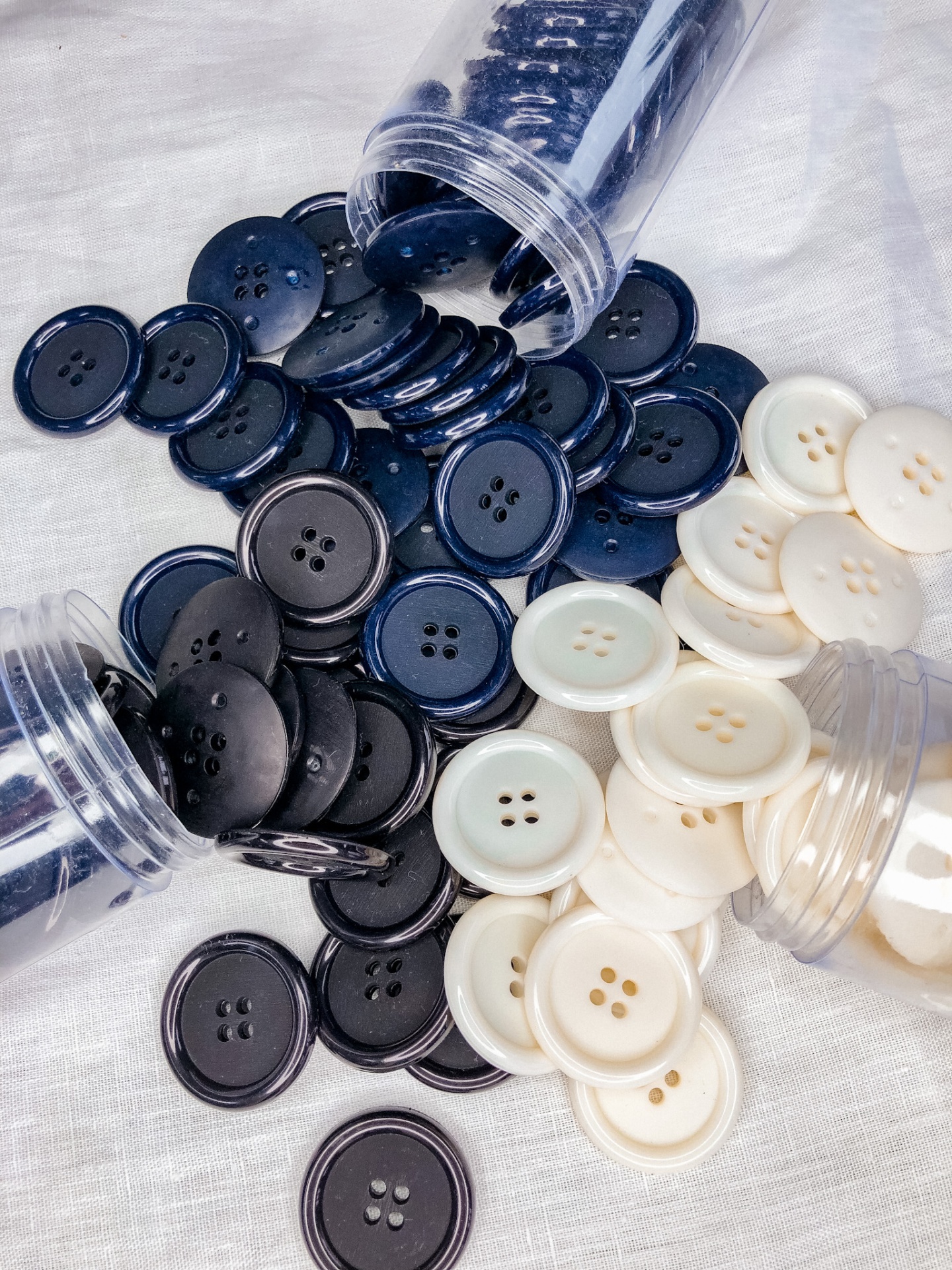 Três frascos transparentes com botões pretos, azuis e brancos sobre tecido branco