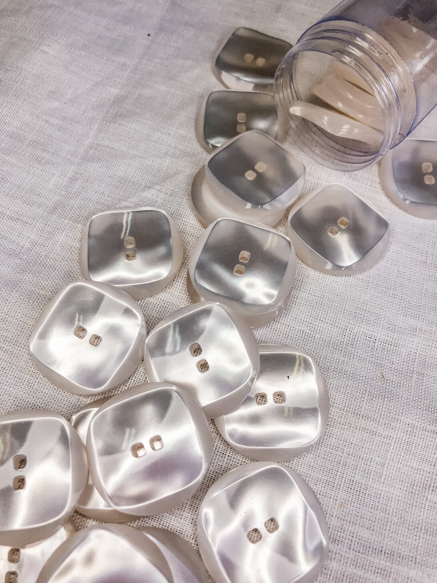 Botões quadrados perolados brancos sobre tecido branco com frasco plástico