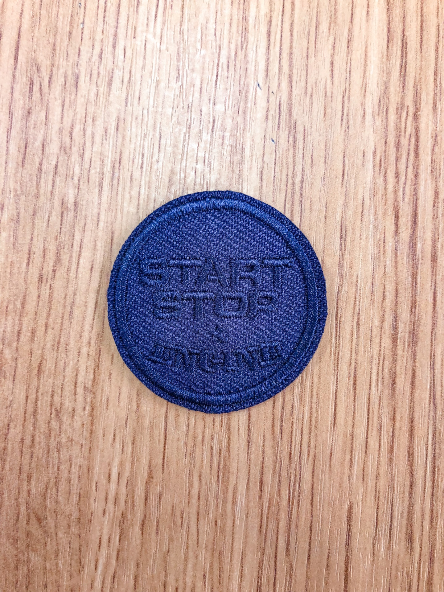 Etiqueta azul-escuro redonda com palavras bordadas sobre madeira clara