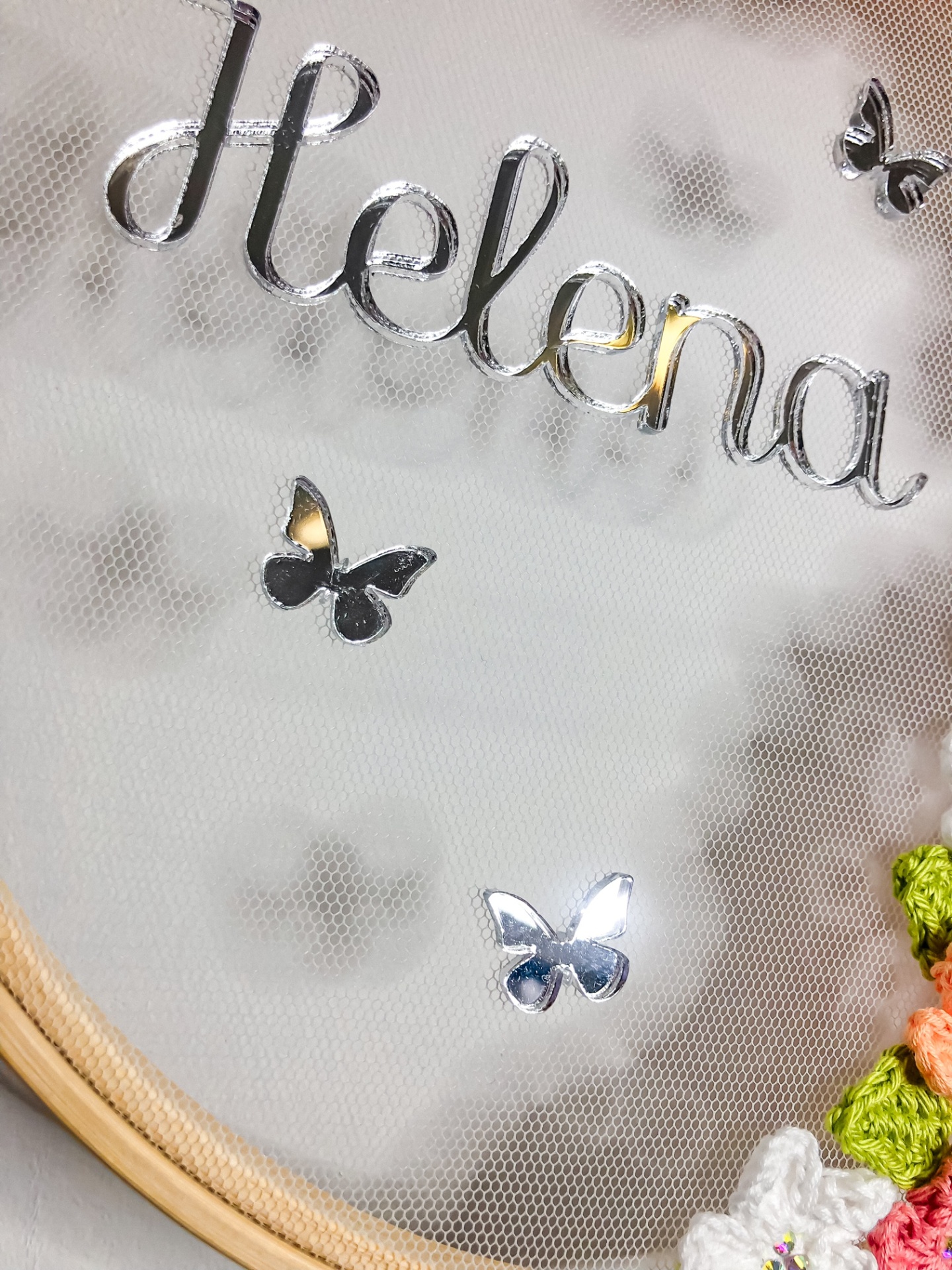 Painel decorativo com nome 'Helena' e borboletas metálicas em tecido de rede dentro de aro de madeira