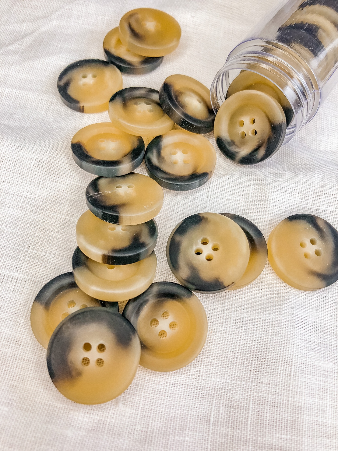Botões plásticos amarelos e pretos com quatro furos sobre tecido branco e frasco transparente