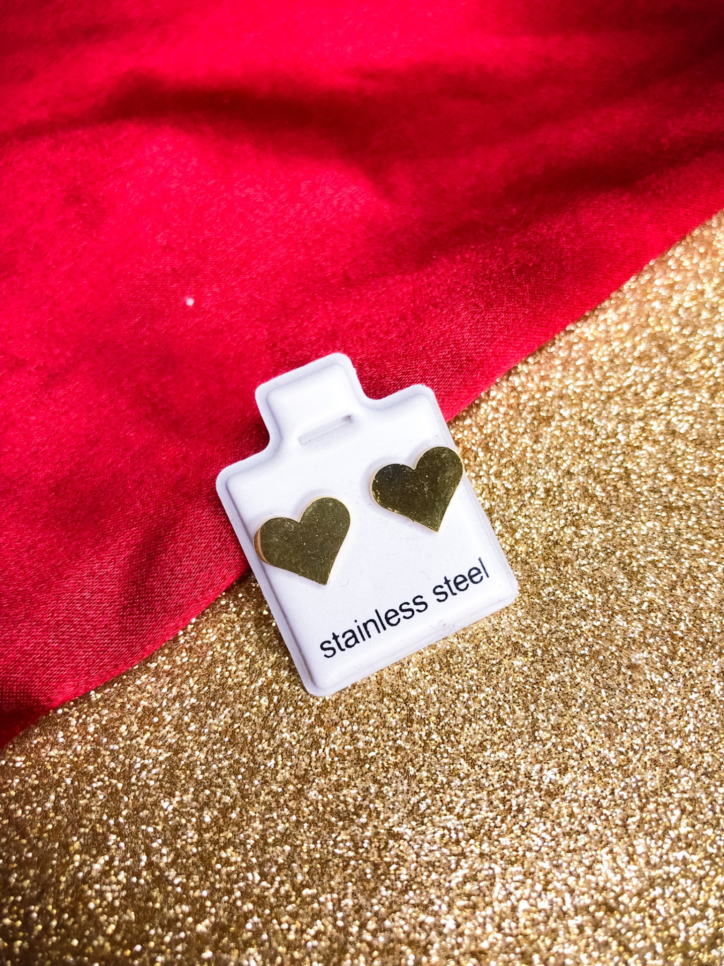 Brincos em forma de coração dourado em aço inoxidável num suporte branco