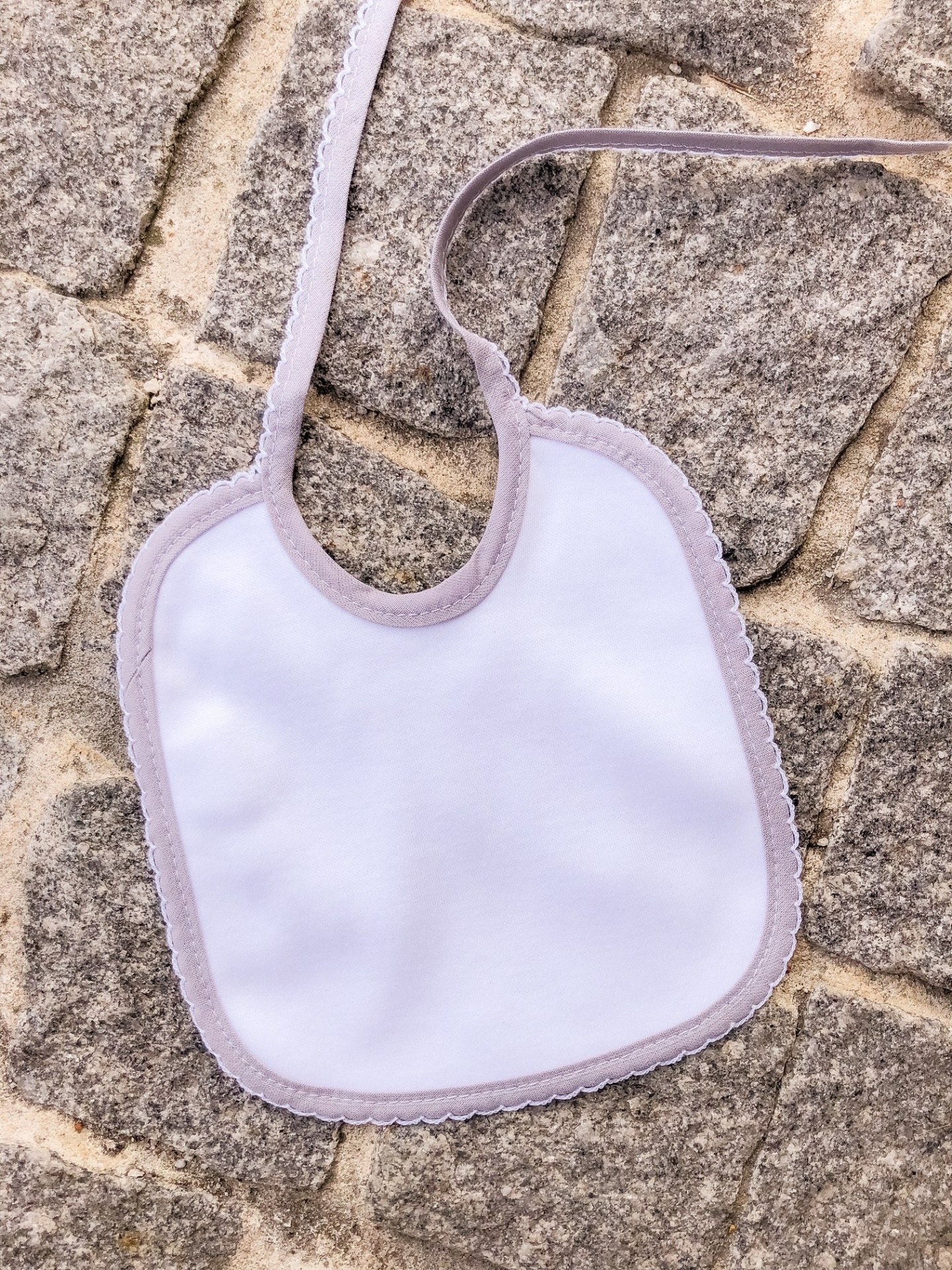 Babete para bebé branco com borda cinzenta claro sobre pedras