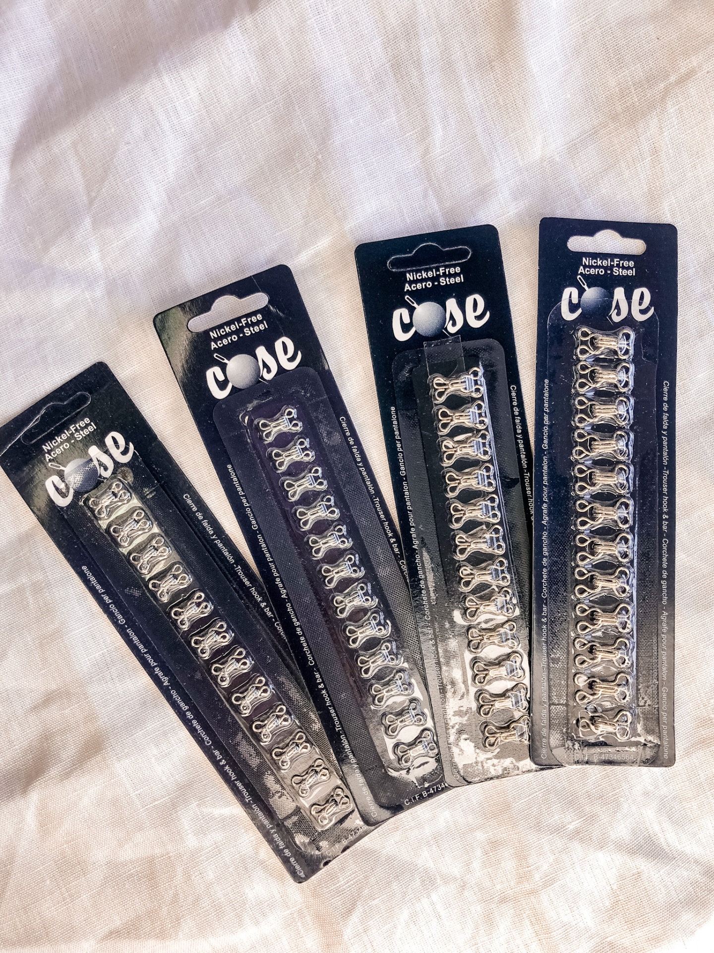 Quatro conjuntos de ganchos e olhos em aço prateado embalados em cartão preto